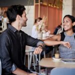 man in black shirt elbow bumping with woman in a restaurant