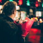 man in black faux fur coat holding bouquet of floweers