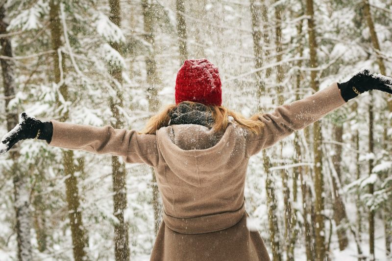 woman wearing hoodie spreading her arm near trees with snows